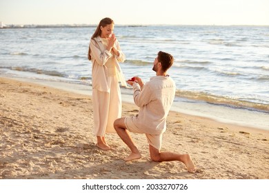 love and people concept - smiling young man with engagement ring making proposal to happy woman on beach - Powered by Shutterstock