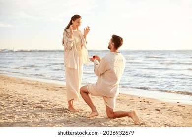 love and people concept - smiling young man with engagement ring making proposal to happy woman on beach - Powered by Shutterstock