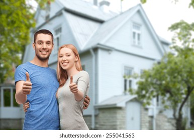 Love, People, Real Estate, Home And Family Concept - Smiling Couple Hugging And Showing Thumbs Up Over House Background