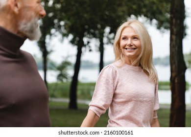 Love And Relationship. Caucasian Mature Couple Walking Together On A Date, Looking At Each Other, Holding Hands In City Park Outdoors.