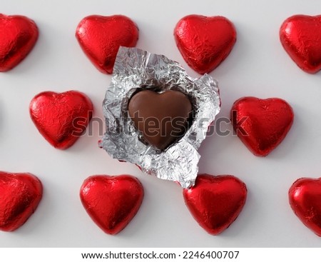 Love and relationship concept - close up of wrapped and unwrapped heart shape chocolate candies in red foil over white background