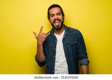 I love rock and roll. Fun young man listening to rock music and sticking his tongue out