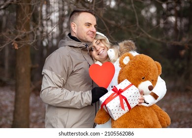 Love and romance. Happy date of couple in love inwinter forest on Valentine's Day. Red heart is symbol of holiday, in hands of woman gift and Teddy bear. Gifts and surprises. Moments of love. 