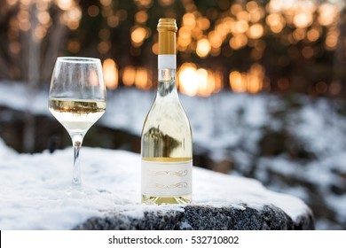 Love, Romance, Holiday, New Year Celebration Concept. Bottle And Glass Of White Wine Chilled By Snow In Winter Forest On Sunset.