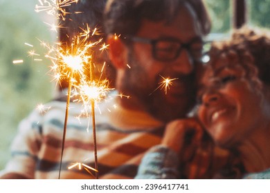 Love and romantic leisure activity with man and woman holding fire sparkler light together hugging and enjoying relationship at home sitting on a sofa. Christmas time for happy couple alone indoor - Shutterstock ID 2396417741