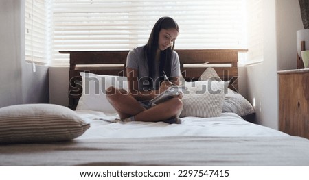 I love seeing the things I manifest come to fruition. a young woman sitting in bed while writing in her diary at home.