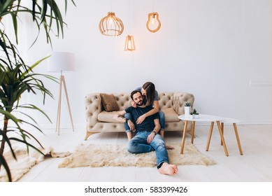 Love story. Beautiful couple sit on sofa, in a large, light interior room. Family, love, tenderness. Side view