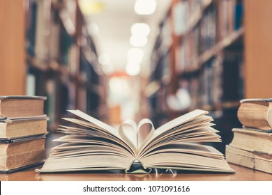 Love story book with open page of literature in heart shape and stack piles of textbooks on reading desk in library, school study room for national library lovers month  and education learning concept