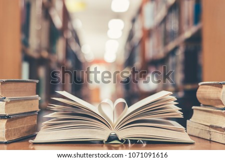 Love story book with open page of literature in heart shape and stack piles of textbooks on reading desk in library, school study room for national library lovers month  and education learning concept