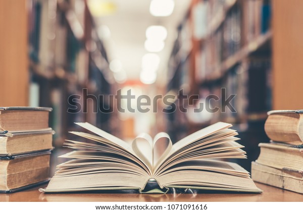 Love story book with open page of literature in\
heart shape and stack piles of textbooks on reading desk in\
library, school study room for national library lovers month  and\
education learning concept