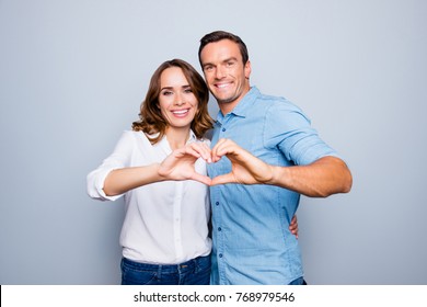 Love Story Of Cheerful, Attractive, Mature, Adult, Lovely, Cute, Sweet Couple In Casual Outfit, Jeans, Shirt Making Heart With Fingers Over Grey Background