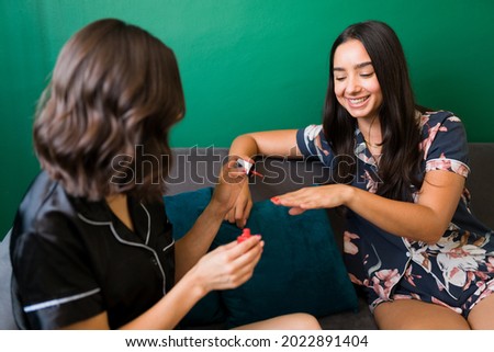 I love this new color. Smiling young woman in pjs getting her nails done by her beautiful best friend while talking about gossip