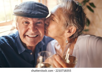 Love, Toast And Old Couple Kiss With Champagne In Celebration Of A Happy Marriage Anniversary Together At Home. Smile, Romance And Senior Woman Enjoying A Relaxing Wine Date And Drink Elderly Partner