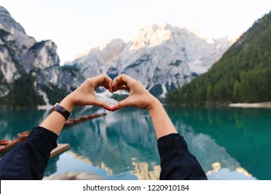 Love to travel and adventure. Woman hiker shows heart sign on background of Dolomites Mountaines. landscape of Braies Lake (Lago di Braies), hiking in alpine lake, Alps, Dolomites, Italy, Europe