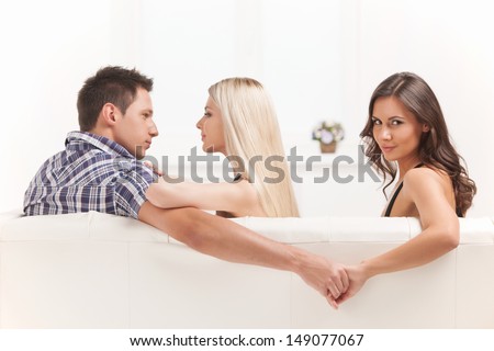 Love triangle. Beautiful young women holding hands with men sitting near his girlfriend