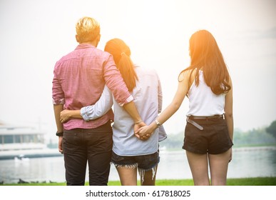 Love triangle, Man is hugging a woman and he is holding hands with another girl,standing outdoor in the park.