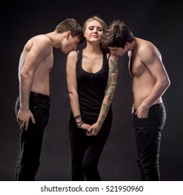 Love triangle. Young woman posing with two young man on a dark background in studio