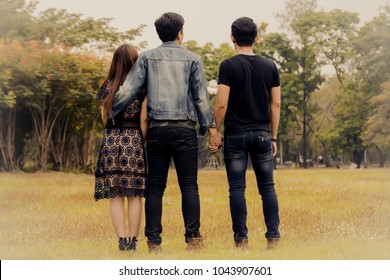 Love triangle. Young woman in relationship with two men.back view of threesome love friends of two men and one woman.