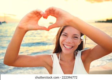 Love vacation - woman showing heart on beach. Girl gesturing heart shaped hands smiling happy and loving at camera. Pretty joyful multicultural Asian Caucasian girl. - Powered by Shutterstock