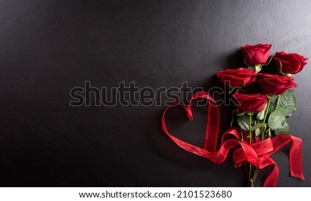 Love and Valentine's day concept made from red rose  and heart ribbon on black wooden background. Top view with copy space, flat lay.