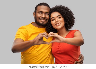 love, valentines day and people concept - happy african american couple making hand heart gesture over grey background