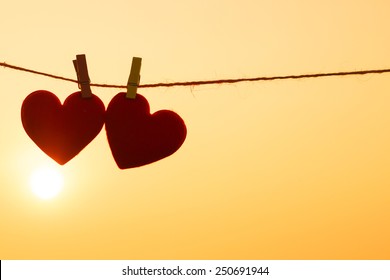Love for Valentine's day - Two red hearts hung on the rope together with sunset silhouette