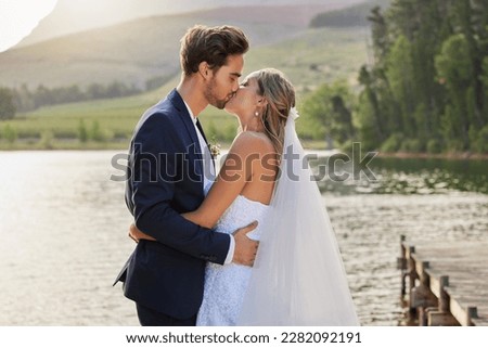 Love, wedding and a married couple kissing by a lake outdoor in celebration of their marriage for romance. Water, summer or kiss with a bride and groom bonding together in tradition after ceremony