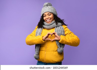 I Love Winter. Cheerful Black Woman Gesturing Heart Shape Smiling To Camera Posing Over Purple Studio Background, Wearing Warm Clothes. Love, Romance, Happy Winter Season Concept