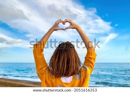 I love you above all things! Young woman on the beach draws a heart with her hands by raising her arms to the sky. Lovely memories to be cherished. 