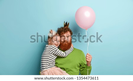 I love you, dad! Bearded redhead father plays with cute little girl, holds balloon, recieves hug from female child, dressed in festive clothes, celebrate Childrens Day together. Family relationships