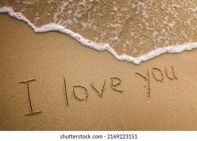 I Love You handwritten on the beach sand with a surging wave. 