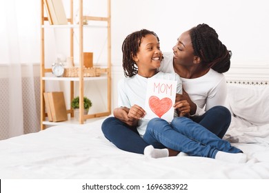 I Love You, Mommy. Happy Black Mother Hugging Her Little Daughter And Holding Greeting Card, Sitting On Bed, Free Space