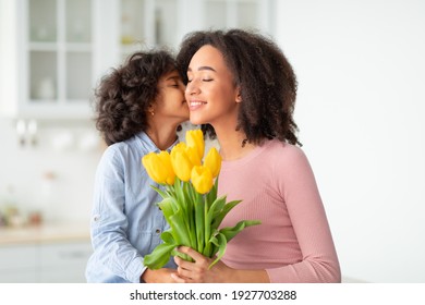 I Love You, Mommy. Portrait of cute African American girl kissing her mum in cheek and giving bunch of yellow tulips flowers, greeting woman with holiday, Women's or Mother's Day or birthday.