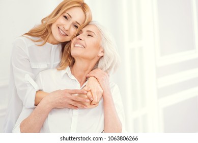 Love you to the moon and back. Full of love charming blonde lady smiling into the camera while standing next to her beautiful mother and hugging her tightly to express her love.
