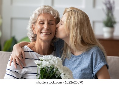 I Love You So Much, My Dear! Affectionate Millennial Daughter Greeting Happy Senior Elderly Mom With Mothers Day, Happy Grandma Receiving Tender Kiss And Flowers With Closed Eyes From Grown Grandkid