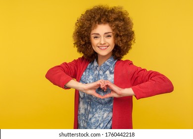 Love You! Portrait Of Romantic Beautiful Woman With Curly Hair Showing Heart Gesture And Smiling Kindly, Expressing Care, Hope And Generosity Symbol. Indoor Studio Shot Isolated On Yellow Background