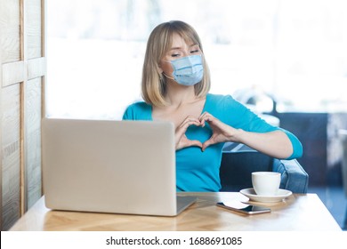 I Love You. Portrait Of Young Woman With Surgical Medical Mask Sitting And Looking At Laptop Display With Heart Gesture On Video Call. Indoor Distance Working, Medicine And Health Care Concept.