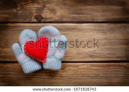 I love you recognition, valentine's day, mother's day, birthday card design. Love and romantic winter concept. Baby mittens and a red felt heart with white stitches on a brown wood wall. 