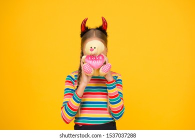 Love you. Small child cover face with teddy bear toy. Little girl in red devil horns hold valentines toy. Plaything. Toy shop. Shopping for Halloween novelty toy.
