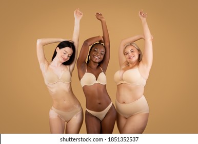 Love Your Body. Happy Three Women With Different Shapes And Appearance Posing Over Beige Studio Background, Positive Beautiful Multi-Ethnic Ladies In Underwear Enjoying Themselves, Copy Space