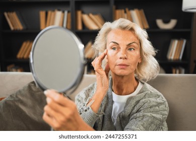 Love yourself. Beautiful old mature woman enjoying mirror reflection. Senior adult older lady looking at mirror confident happy on sofa at home. Woman doing daily morning beauty routine. Self love - Powered by Shutterstock