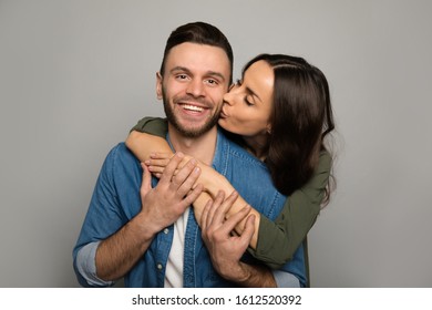 Loved one. Сlose-up photo of a charming lady with chestnut hair, who is kissing her handsome boyfriend in the cheek, while hugging him from the back.