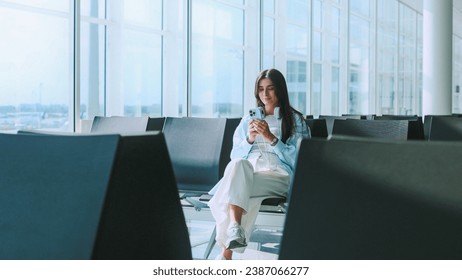 Lovely and adorable Caucasian lady sitting at airport waiting for departure. Charming and gorgeous young woman using smartphone online communicating. Traveling concept. - Powered by Shutterstock