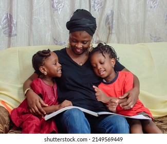 Lovely African Nigerian Family Consisting Of A Mother Or Guardian And Two Little Girl Child, Sitting Curdled Together As They Happily Study Altogether