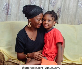 Lovely African Nigerian Family Consisting Of A Mother Or Guardian And Her Little Girl Child, Sitting Cuddled Together As They Happily Play Together