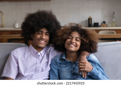 Lovely African Teenager, Smiling Girl And Guy Sit On Sofa Look At Camera, Spend Time Together At Home. Portrait Of Friendly Roommates In Good Relations, First Romantic Relationships, Couple In Love