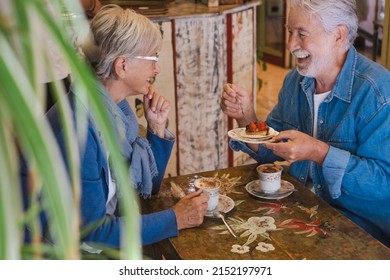 Lovely Amused Senior Couple Inside A Coffee Shop Having Breakfast With Fruit Cake And Cappuccino. Two Elderly People Enjoying Retirement And Stay Together