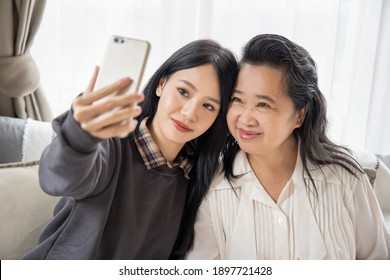 Lovely asian senior mother and young daughter taking smartphone photo selfie with happy family life, single mom, togetherness concept
