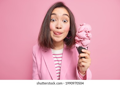 Lovely Asian Woman With Dark Hair Licks Lips Starves To Eat Ice Cream Likes Sweet Junk Food Dressed Formally Isolated On Pink Background. Summer Time Concept. Pretty Female Model Likes Frozen Dessert