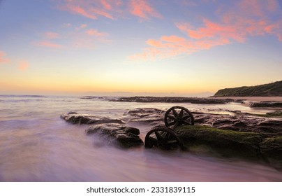 Lovely autumn sunrise over Windang Beach with one of the many abandoned rusty train wheels exposed on mossy rocks at low tide. - Powered by Shutterstock